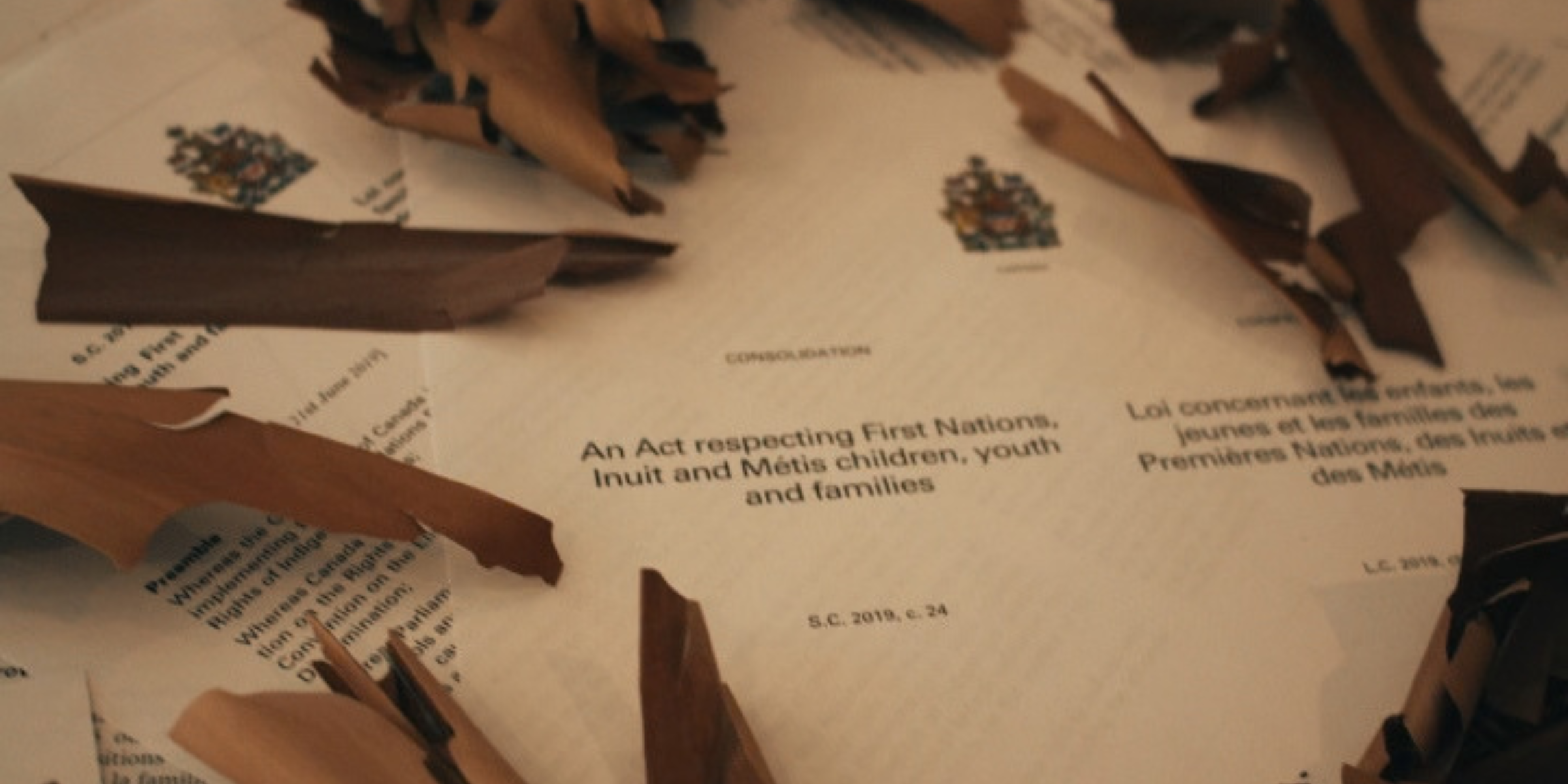 scattered pages of An Act Respecting First Nations, Inuit and Metis children youth and families surrounded by birch bark