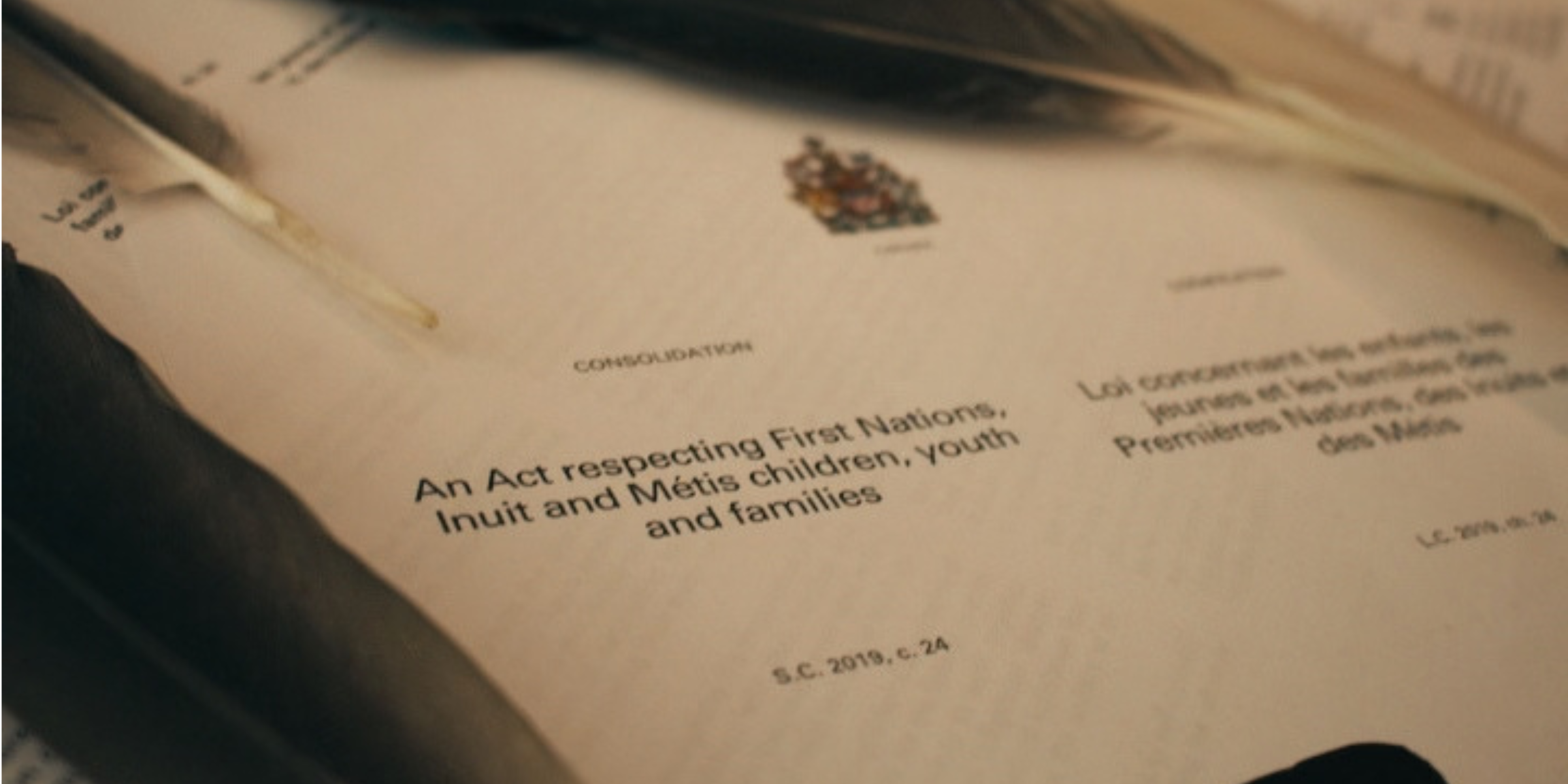 scattered pages of An Act Respecting First Nations, Inuit and Metis children youth and families surrounded by eagle feathers